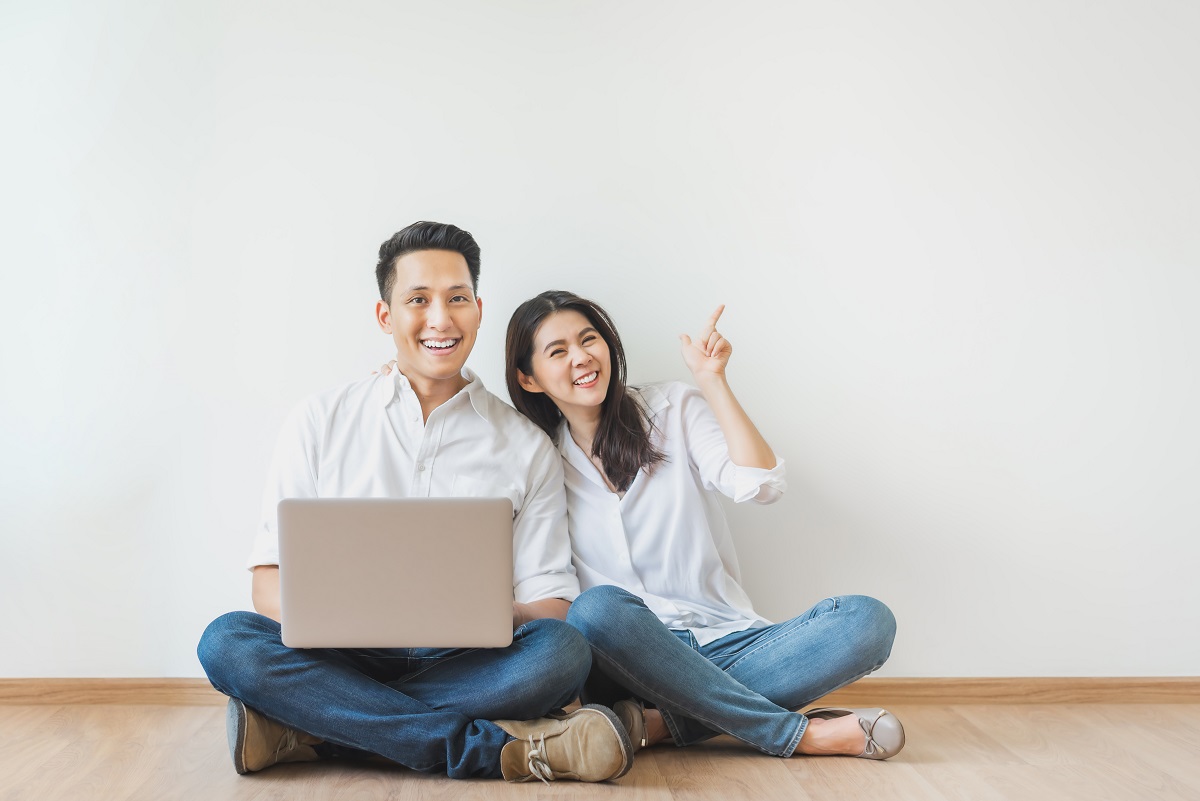 Asian Couple Sitting On Floor Using Laptop In White Room