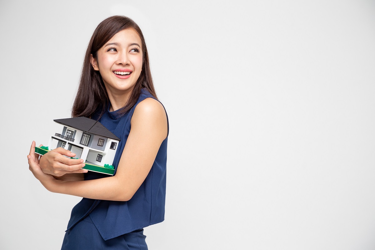 Young Asian Woman Smiling And Hugging Dream House Sample Model Isolated Over White Background, Real Estate And Home Insurance Concept