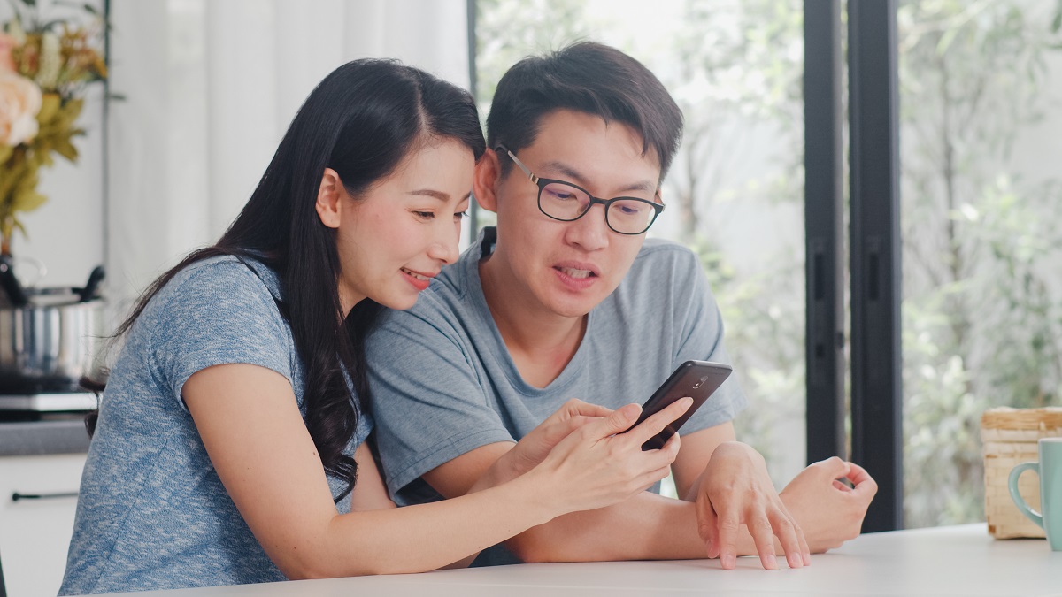Young Asian Couple Enjoy Shopping Online On Mobile Phone At Home